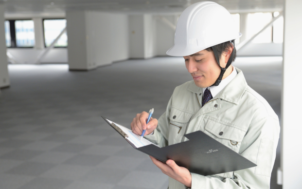 Construction Worker with hard hat inspecting plans on a clipboard in an open warehouse
